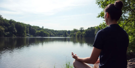 Person meditating by a lake in a peaceful natural setting.